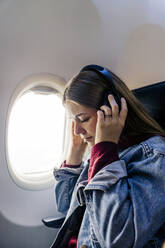 Junge Frau, die im Flugzeug mit Kopfhörern Musik hört - JJF00879