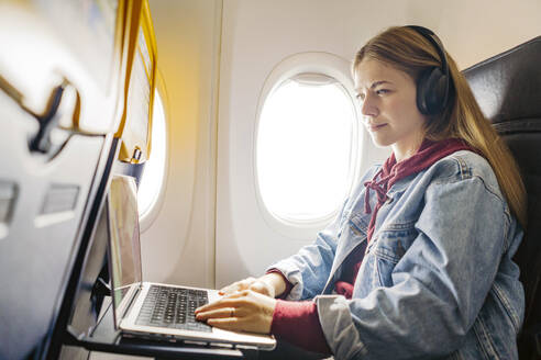 Junge Frau benutzt Laptop und hört Musik im Flugzeug - JJF00882