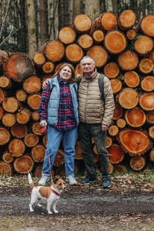 Älteres Paar mit Hund vor Kiefernstämmen im Wald stehend - VSNF00749