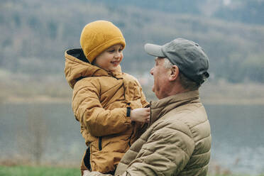 Grandfather carrying grandson wearing warm clothing - VSNF00751