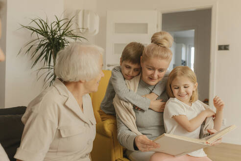 Ältere Frau sitzt mit Tochter und Enkelkindern und schaut sich zu Hause ein Fotoalbum an - VIVF00575