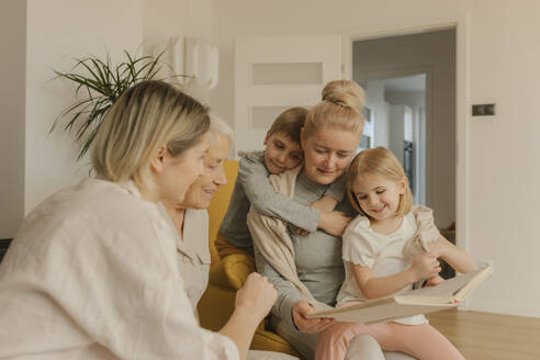 Mehrgenerationen-Familie, die zu Hause sitzend ein Fotoalbum betrachtet - VIVF00576
