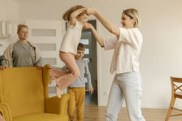 Mother assisting daughter jumping from armchair at home - VIVF00584