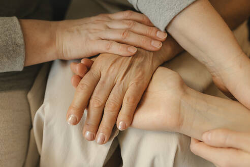 Elderly woman stacking hands with family at home - VIVF00588