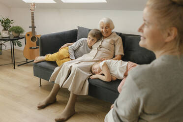 Großmutter sitzt mit Enkelkindern auf dem Sofa zu Hause - VIVF00593