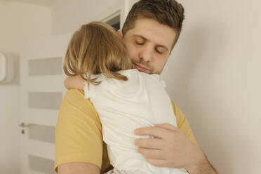 Father with eyes closed embracing daughter at home - VIVF00613