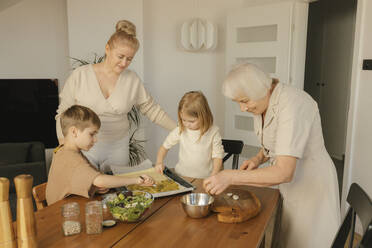 Enkelkinder bei der Essenszubereitung mit Mutter und Großmutter zu Hause - VIVF00636
