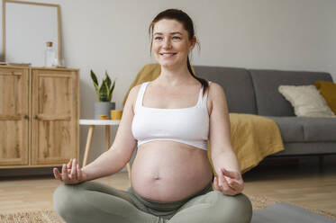 Lächelnde schwangere Frau macht Yoga zu Hause - ALKF00195