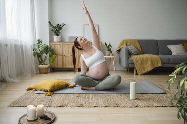 Pregnant woman doing Yoga with hand raised at home - ALKF00196