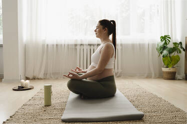 Schwangere Frau meditiert auf einer Übungsmatte zu Hause - ALKF00198