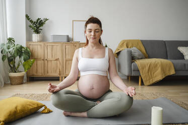 Pregnant woman with eyes closed meditating on exercise mat at home - ALKF00200