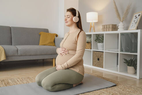 Schwangere Frau beim Musikhören auf einer Gymnastikmatte zu Hause - ALKF00214