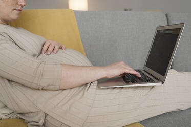 Pregnant freelancer typing on laptop at home office - ALKF00231