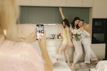 Woman photographing friends enjoying in kitchen at home - VIVF00648