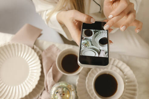 Frau fotografiert Kaffee mit ihrem Smartphone zu Hause - VIVF00654