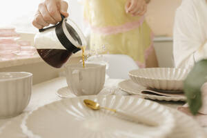 Frau gießt Kaffee in eine Tasse am Tisch im Haus - VIVF00655