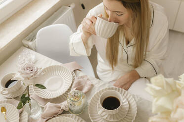 Frau trinkt schwarzen Kaffee am Tisch sitzend im Haus - VIVF00657