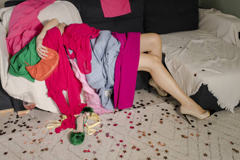 Woman embracing heap of clothes lying on sofa at home - VIVF00731