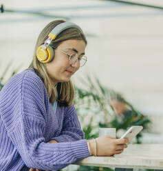 Lächelndes Mädchen, das über drahtlose Kopfhörer in der Schulcafeteria sitzt und Musik hört - VSNF00755