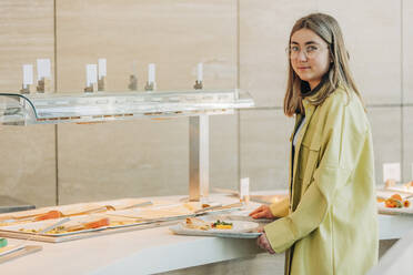 Teenage girl holding tray near buffet at school cafeteria - VSNF00758