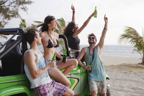 Happy friends enjoying drinks with off-road vehicle at beach - IKF00273