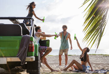 Fröhliche Freunde stoßen mit Getränkeflaschen im Geländewagen am Strand an - IKF00274