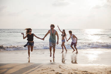 Glückliche Freunde halten Hände und spielen am Strand - IKF00278
