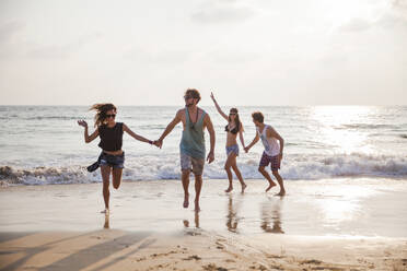 Happy friends holding hands and playing at beach - IKF00278