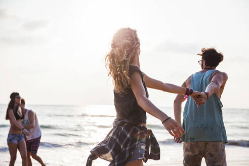 Carefree friends holding hands and playing at beach - IKF00279