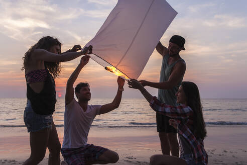 Freunde brennen Papierlaterne bei Sonnenuntergang Strand - IKF00285