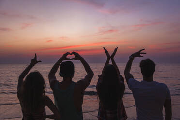 Freunde machen Liebe Text Zeichen mit Händen am Strand bei Sonnenuntergang - IKF00290