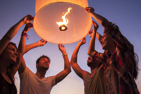 Smiling friends holding illuminated paper lantern - IKF00291