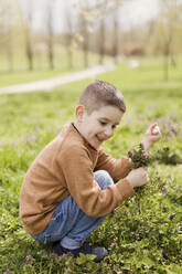 Lächelnder Junge mit Blumen in der Hand im Park hockend - ONAF00507