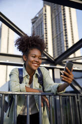 Lächelnde Frau, die ein Selfie mit ihrem Smartphone macht und sich auf ein Geländer stützt - IKF00302
