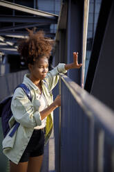 Young woman shielding eyes standing on bridge - IKF00306