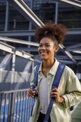 Contemplative young woman with backpack standing on bridge - IKF00321