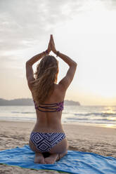 Junge Frau im Bikini übt Yoga mit verschränkten Händen am Strand - IKF00330