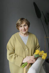 Elderly woman standing with flowers in hand at home - OGF01286