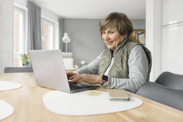 Lächelnde Frau mit Laptop auf dem Tisch zu Hause - OGF01287