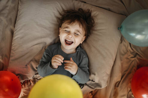 Junge lachend inmitten von Luftballons auf dem Bett - ANAF01273