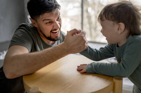 Excited father arm wrestling with son at home - ANAF01283