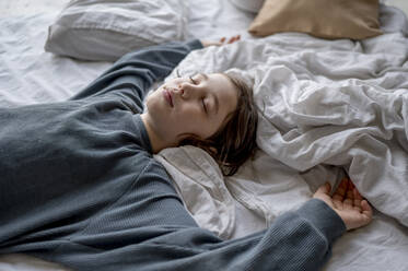 Carefree boy sleeping on bed at home - ANAF01284