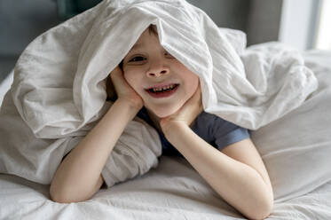 Junge liegt unter einer Decke auf dem Bett zu Hause - ANAF01288