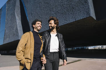 Lächelnde Homosexuell Mann zu Fuß mit Freund in der Nähe von Gebäude an sonnigen Tag - MMPF00722