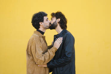 Romantisches schwules Paar küsst sich vor gelbem Hintergrund - MMPF00725