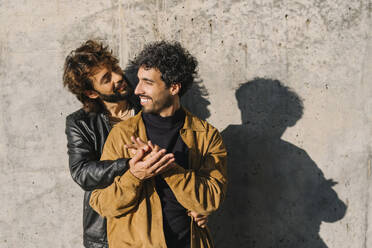 Romantisches homosexuelles Paar steht vor einer Betonmauer an einem sonnigen Tag - MMPF00745