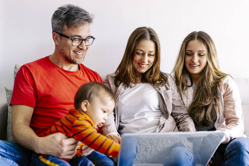 Lächelnde Familie, die gemeinsam zu Hause am Laptop sitzt - JJF00885