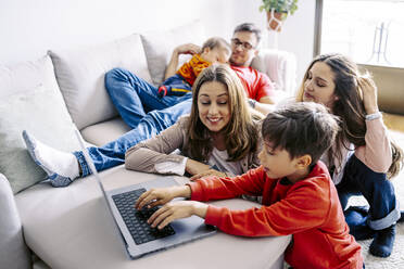 Junge mit Laptop bei der Familie im heimischen Wohnzimmer sitzend - JJF00887
