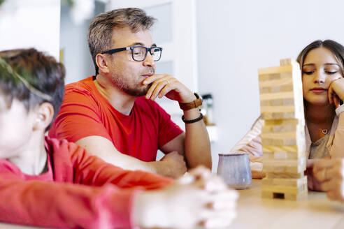 Thoughtful father playing block removal game with family at home - JJF00909