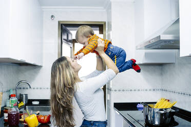 Playful sister picking up baby boy in kitchen at home - JJF00929